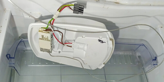 Мастер проводит замену термостата в холодильнике